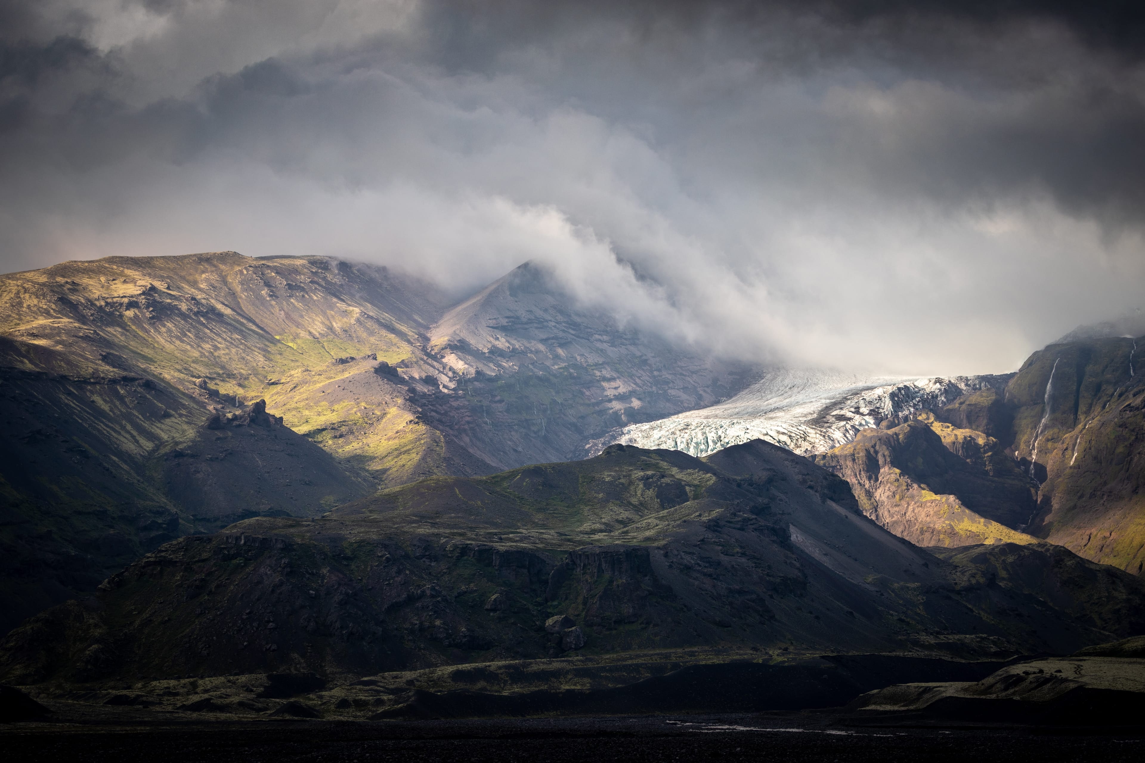 Langue glaciaire au creux d’une vallée volcanique, les nuages s’effilant au-dessus des crêtes